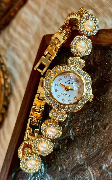 Gold ladies bracelet watch with freshwater pearl and pav´e crystal
flower link chain, scalloped floral case and champagne dial by Le Belle Heure
