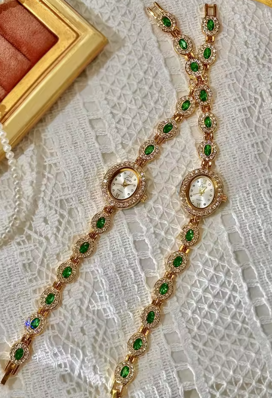 Gold bracelet watch with emerald green oval faceted gemstones set in
white pave crystal halos and champagne oval dial for women by Le Belle Heure