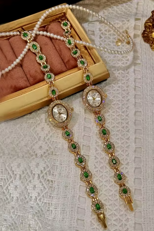 Gold bracelet watch with emerald green oval faceted gemstones set in
white pave crystal halos and champagne oval dial for women by Le Belle Heure