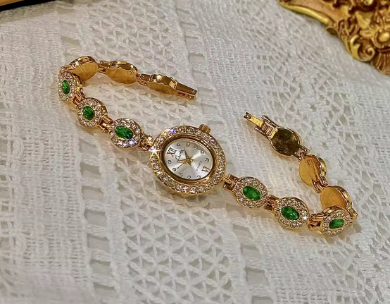 Gold bracelet watch with emerald green oval faceted gemstones set in
white pave crystal halos and champagne oval dial for women by Le Belle Heure
