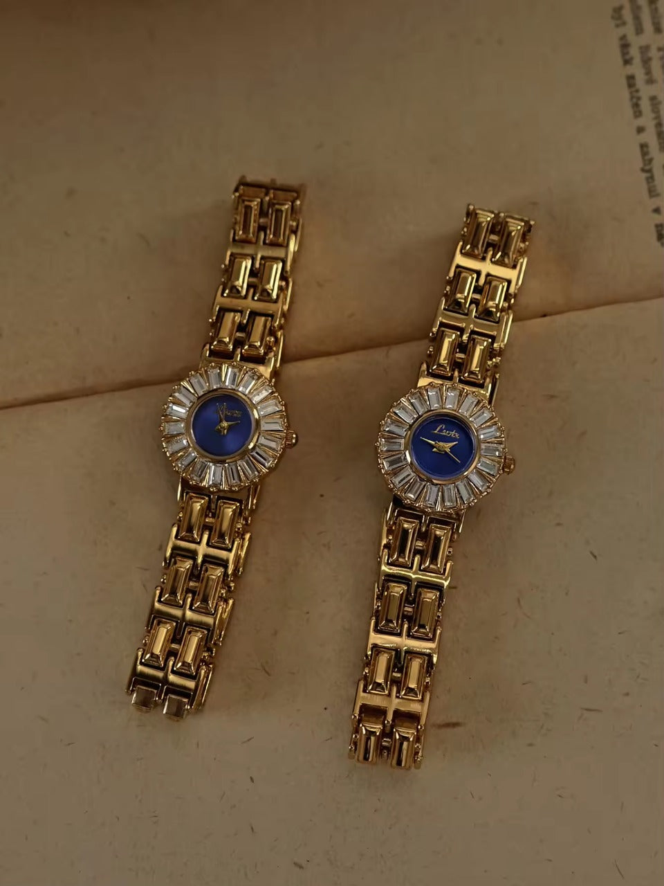 Gold bracelet watch with navy blue dial and baguette crystal starburst
halo bezel on wide panther chain band for women by Le Belle Heure