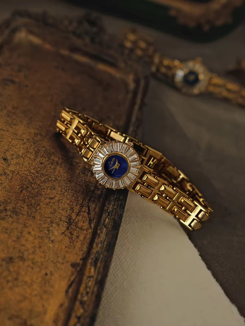 Gold bracelet watch with navy blue dial and baguette crystal starburst
halo bezel on wide panther chain band for women by Le Belle Heure
