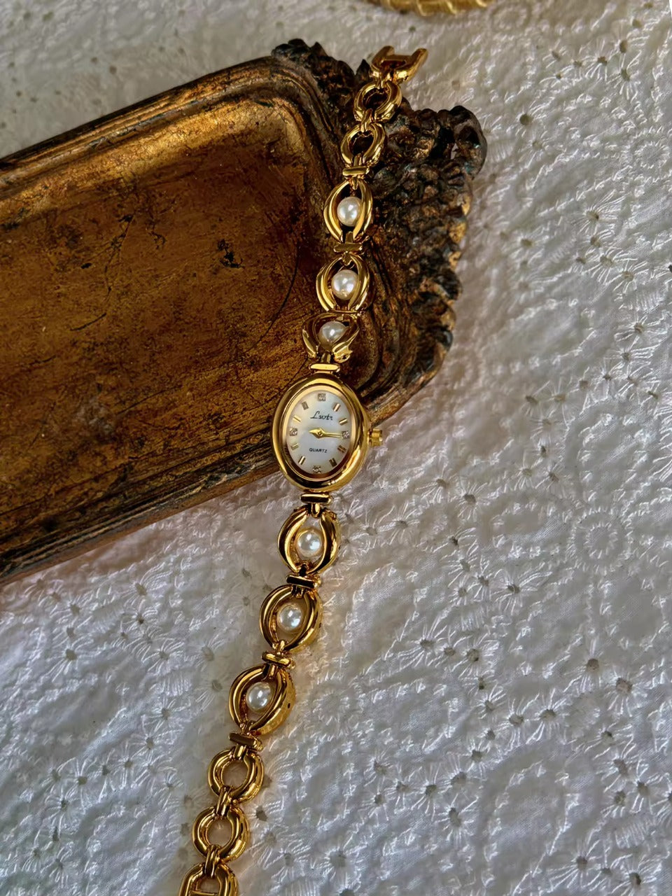 Gold oval bracelet watch with freshwater pearl eye-link chain and
champagne dial with gold hour markers for women by Le Belle Heure