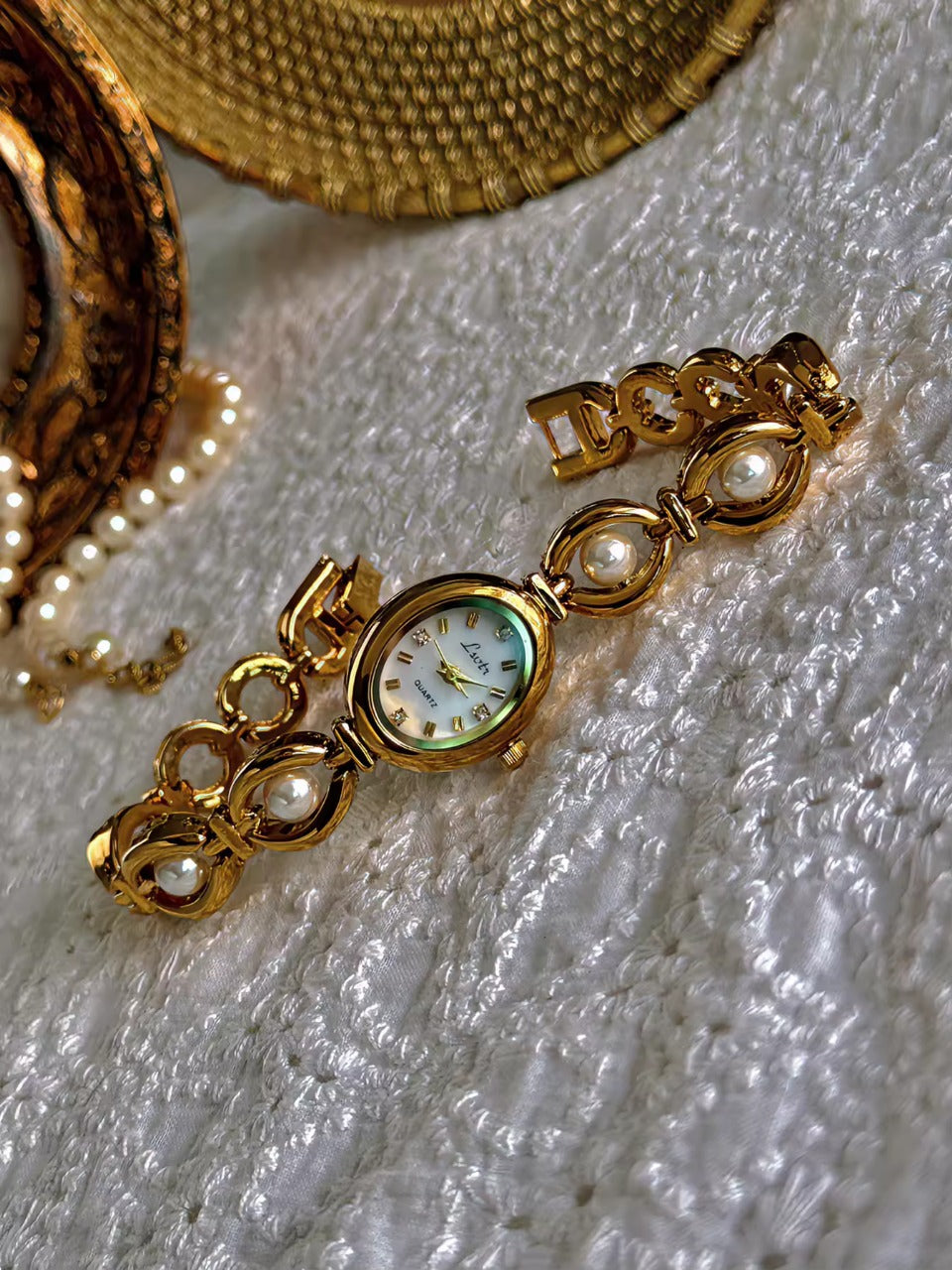 Gold oval bracelet watch with freshwater pearl eye-link chain and
champagne dial with gold hour markers for women by Le Belle Heure