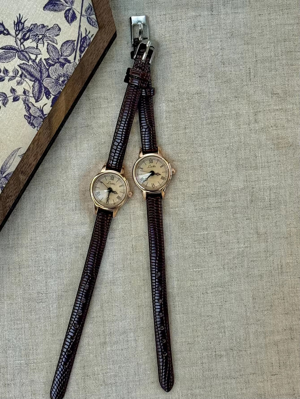 Women’s rose gold Roman numeral watch with brown lizard-grain
leather strap on linen background