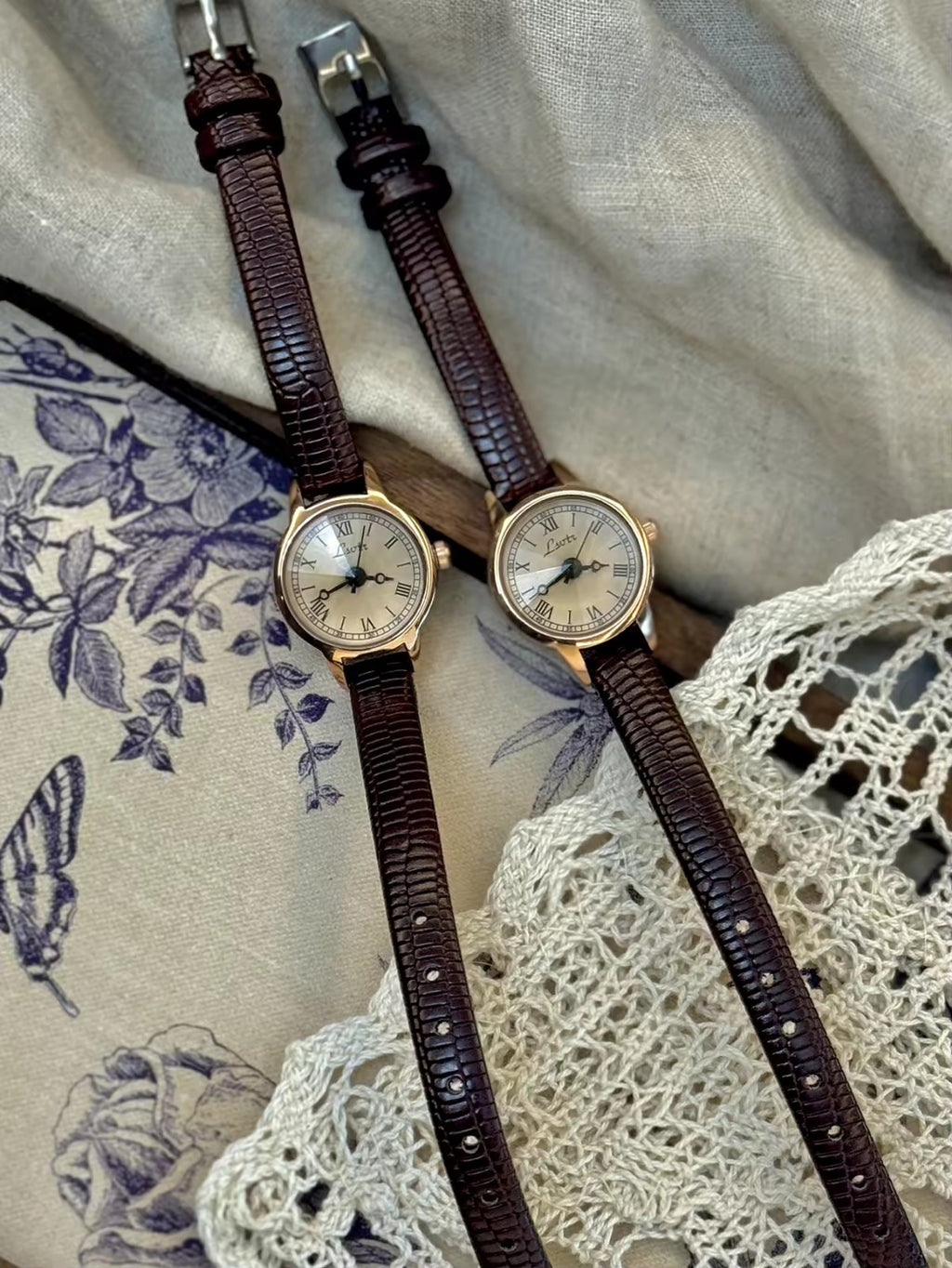 Women’s rose gold Roman numeral watch with brown lizard-grain
leather strap on linen background