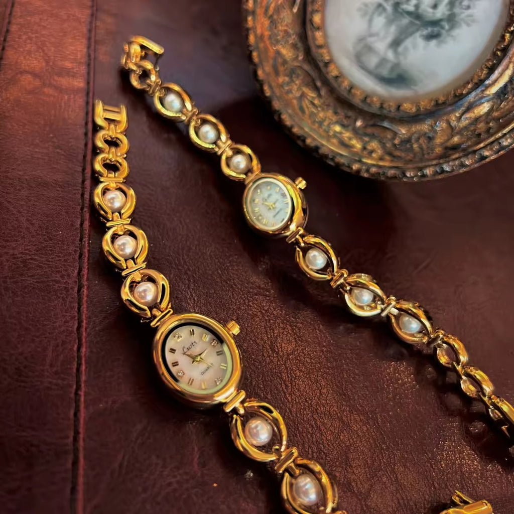 Gold oval bracelet watch with freshwater pearl eye-link chain and
champagne dial with gold hour markers for women by Le Belle Heure
