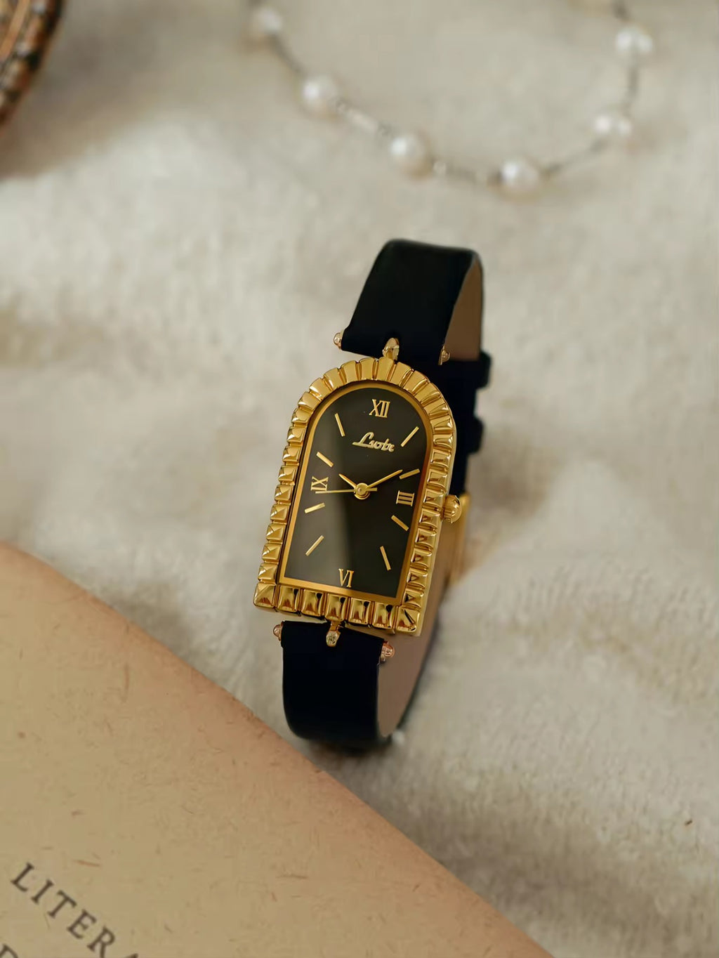 Gold arch-shaped case watch with scalloped fluted bezel, black Roman
numeral dial with gold hour markers and slim black leather strap with gold buckle for women by Le Belle Heure
