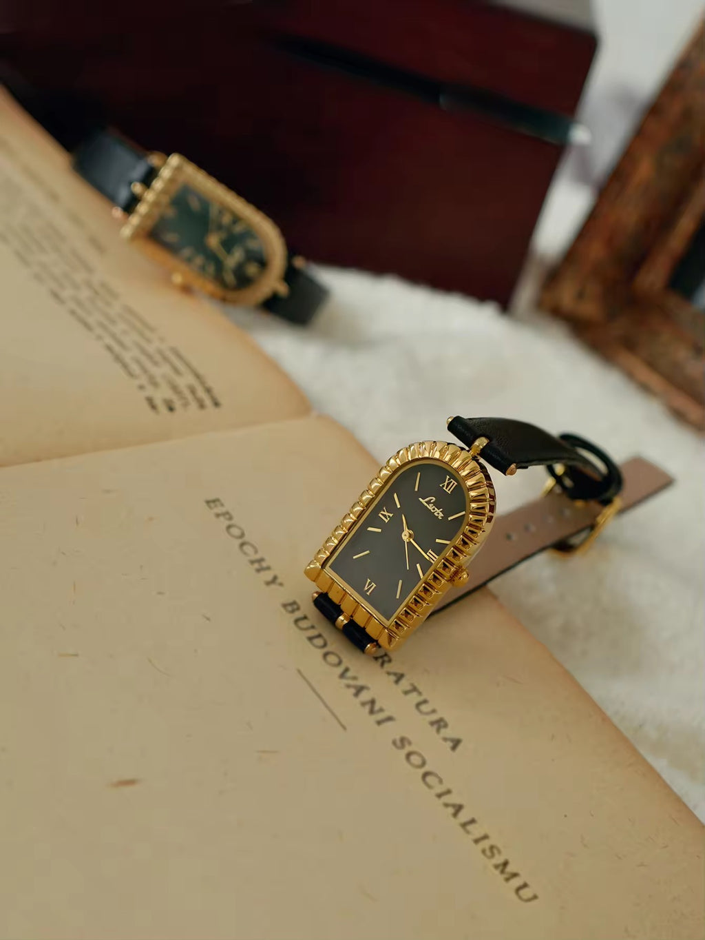 Gold arch-shaped case watch with scalloped fluted bezel, black Roman
numeral dial with gold hour markers and slim black leather strap with gold buckle for women by Le Belle Heure
