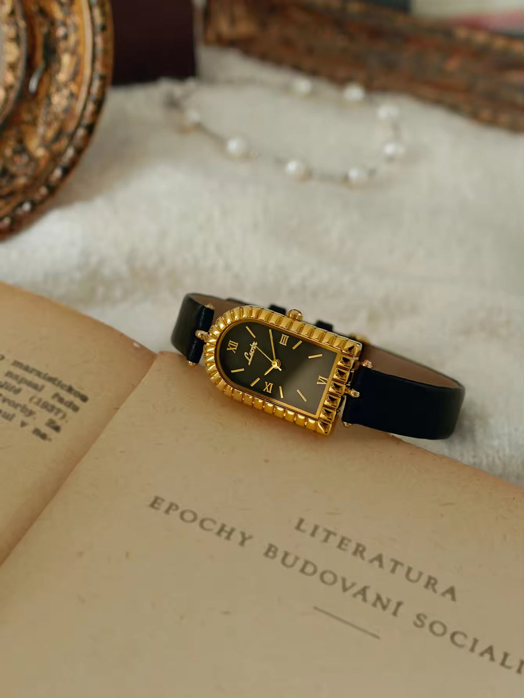 Gold arch-shaped case watch with scalloped fluted bezel, black Roman
numeral dial with gold hour markers and slim black leather strap with gold buckle for women by Le Belle Heure
