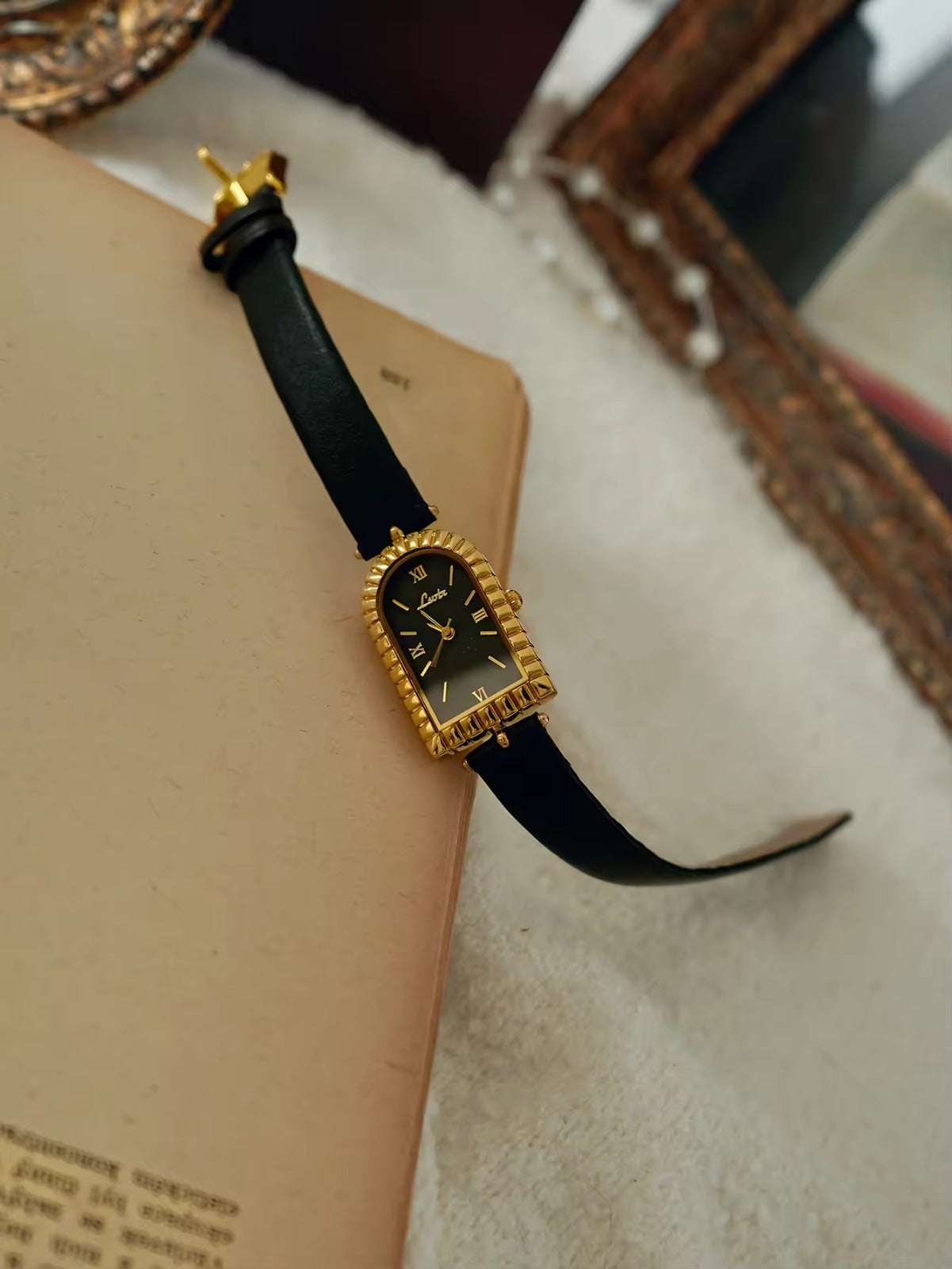 Gold arch-shaped case watch with scalloped fluted bezel, black Roman
numeral dial with gold hour markers and slim black leather strap with gold buckle for women by Le Belle Heure
