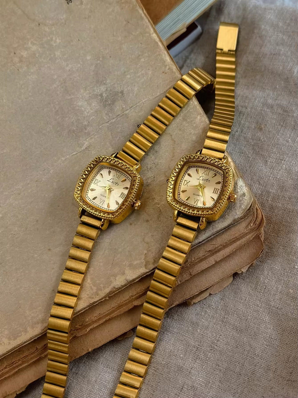 Gold cushion square watch with deeply engraved geometric chevron
bezel, Roman numeral and baton marker champagne dial and structured gold expansion flex bracelet for women by Le Belle Heure