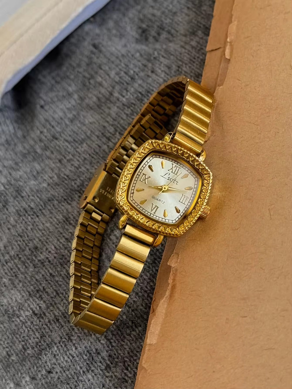 Gold cushion square watch with deeply engraved geometric chevron
bezel, Roman numeral and baton marker champagne dial and structured gold expansion flex bracelet for women by Le Belle Heure