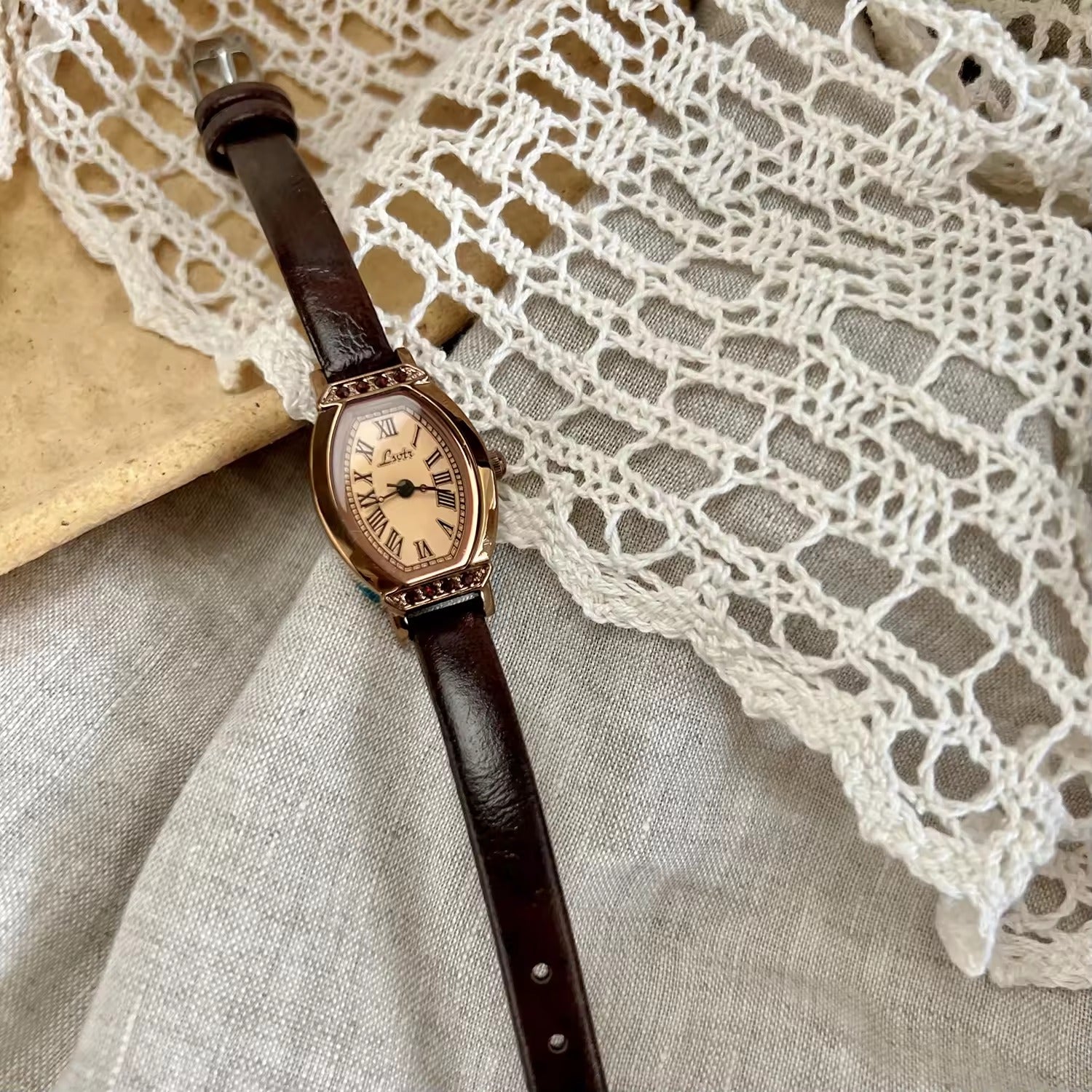 Rose gold tonneau watch with crystal-set upper and lower bezel, ivory champagne Roman numeral dial and slim dark chocolate brown leather strap for women by Le Belle Heure