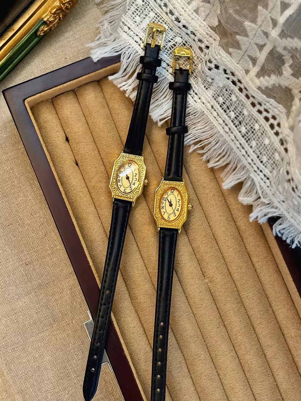 Two women’s vintage gold octagonal watches with engraved filigree bezels, champagne dials, and slim black leather straps on a velvet display tray — Le Belle Heure