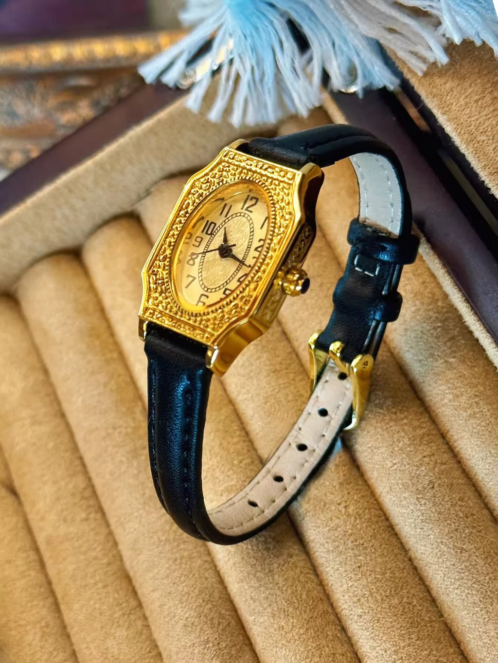 Two women’s vintage gold octagonal watches with engraved filigree bezels, champagne dials, and slim black leather straps on a velvet display tray — Le Belle Heure