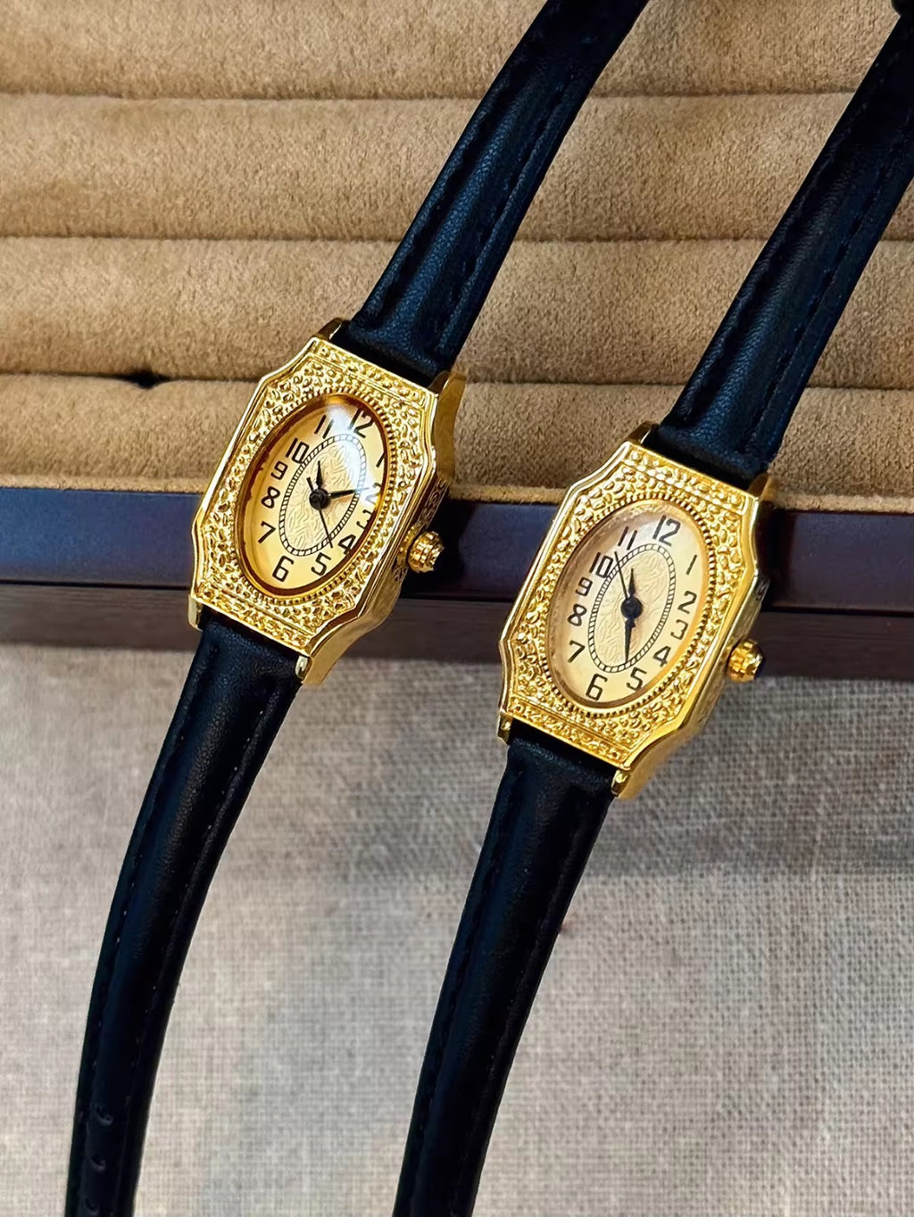 Two women’s vintage gold octagonal watches with engraved filigree bezels, champagne dials, and slim black leather straps on a velvet display tray — Le Belle Heure