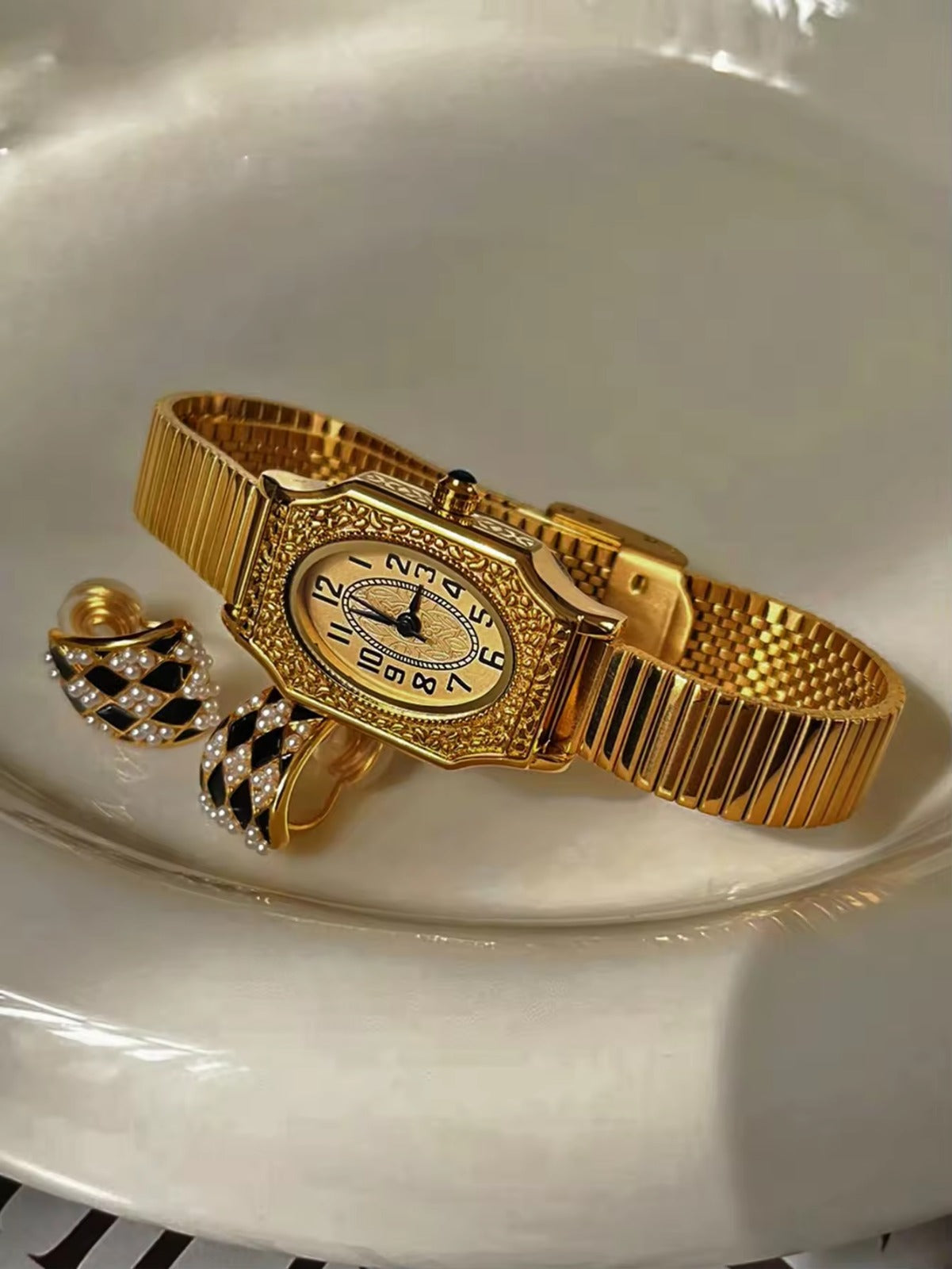 Two women’s vintage gold octagonal watches with engraved filigree bezels, white Arabic numeral dials, and gold accordion ribbed flex bracelets on an antique book — Le Belle Heure