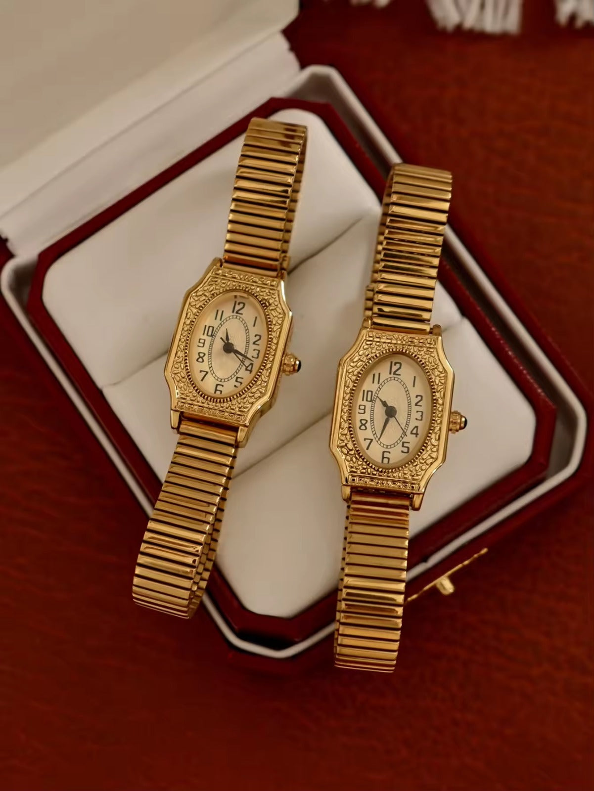 Two women’s vintage gold octagonal watches with engraved filigree bezels, white Arabic numeral dials, and gold accordion ribbed flex bracelets on an antique book — Le Belle Heure