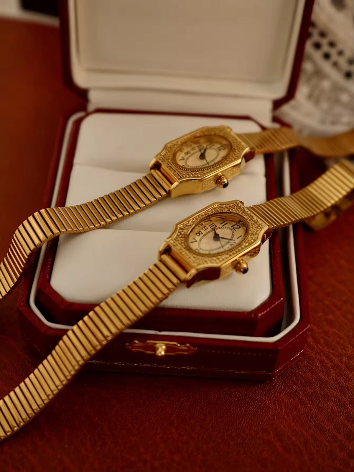 Two women’s vintage gold octagonal watches with engraved filigree bezels, white Arabic numeral dials, and gold accordion ribbed flex bracelets on an antique book — Le Belle Heure