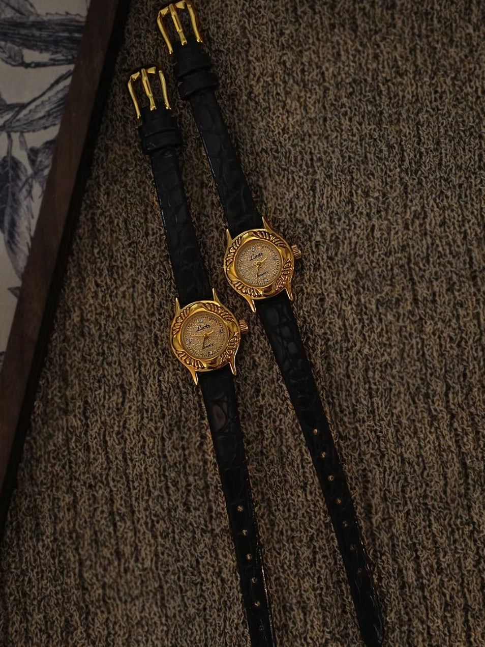 Gold oval watch with deeply engraved feather and leaf floral case,
champagne glitter dial, sculpted gold lugs and slim black crocodile texture leather strap for women by Le Belle Heure”.