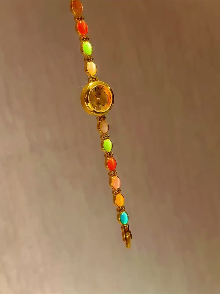 Gold-tone round dial women’s bracelet watch with multicolour peach, green and red oval gemstones by Le Belle Heure
